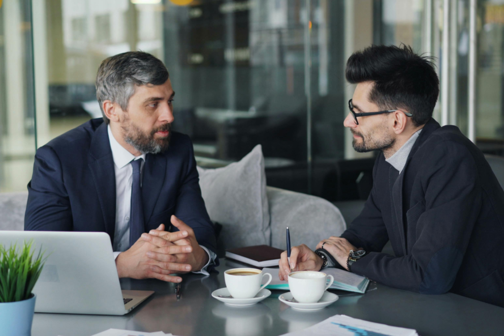 How to talk to your clients switching to voip. This image shows two men in suits sitting down with two coffees in front of them talking to each other. They are presumably having a conversation about switching their VoIP provider.